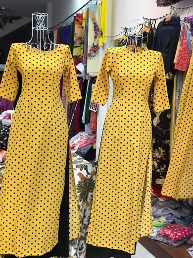 Hai chiếc áo dài đồng phục vàng chấm bi đen trên ma-nơ-canh.