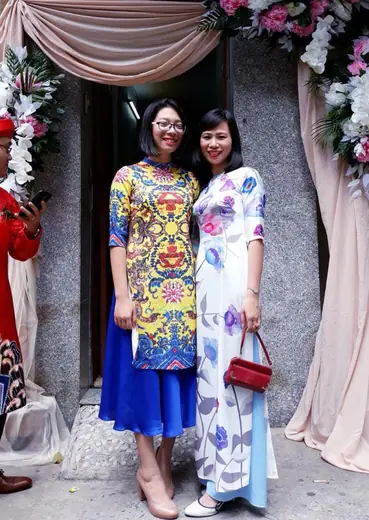 Hai phụ nữ mặc áo dài cách tân chụp gần trước cổng hoa đám cưới.