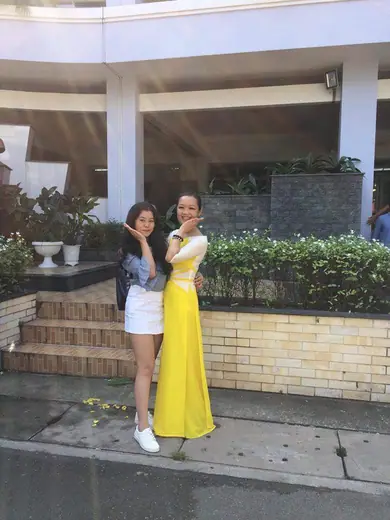Hai phụ nữ đứng trước toà nhà, một người mặc áo dài vàng.
