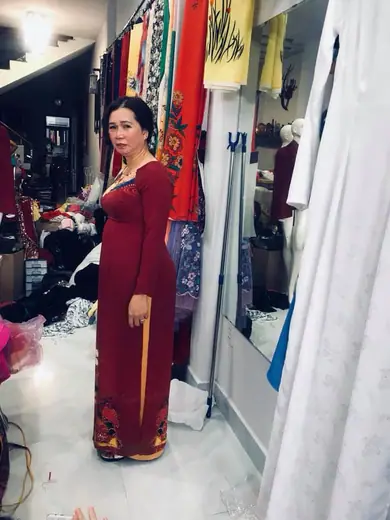 Một phụ nữ mặc áo dài đỏ đô đứng nghiêng trong tiệm.