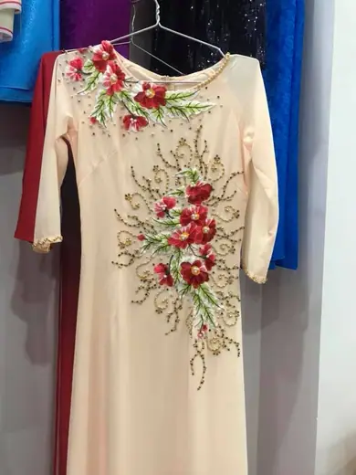 Áo màu kem kết hoa cườm đỏ treo trên móc.