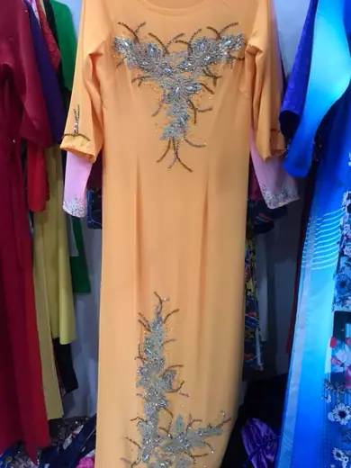 Áo dài màu cam nhạt đính ren xanh xám treo trên móc.