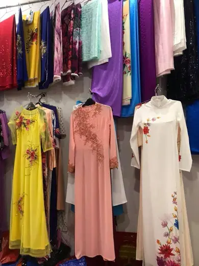 Ba chiếc áo dài vàng, hồng và kem treo trong tiệm.