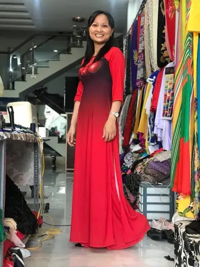 Một phụ nữ mặc thử áo dài đồng phục đỏ chuyển màu đen trong tiệm.