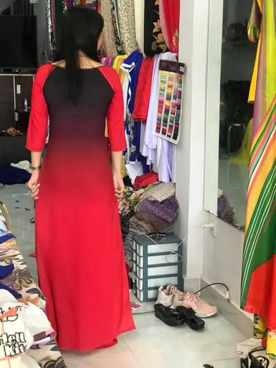 Một phụ nữ mặc áo dài đỏ chuyển đen, nhìn từ phía sau.