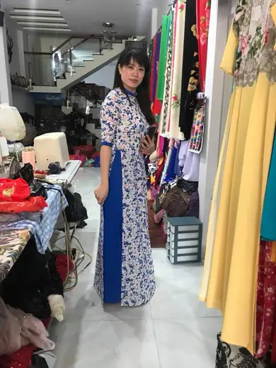 Một phụ nữ mặc áo dài trắng hoa xanh phối tà xanh dương đứng trong tiệm.