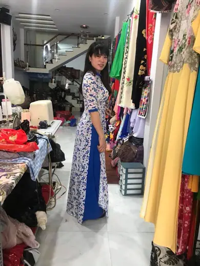Một phụ nữ mặc áo dài trắng hoa xanh phối tà xanh dương trong tiệm.