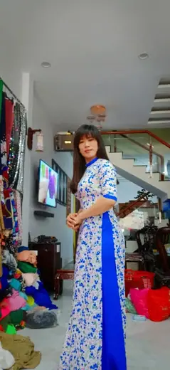 Một phụ nữ mặc áo dài trắng hoa xanh đứng nghiêng trong tiệm.