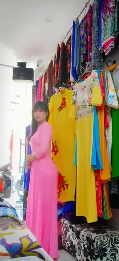 Một phụ nữ mặc áo dài hồng đứng soi gương trong tiệm.