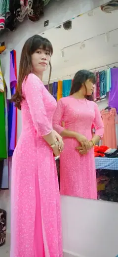 Một phụ nữ mặc áo dài hồng đứng trước gương trong tiệm.