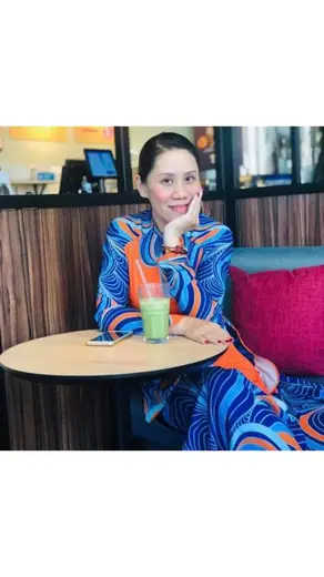 Một phụ nữ mặc áo dài in hoạ tiết xoáy xanh ngồi bên bàn cà phê.