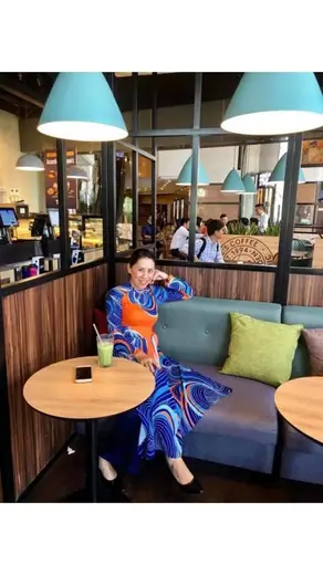 Một phụ nữ mặc áo dài hoạ tiết xoáy xanh ngồi trong quán cà phê.