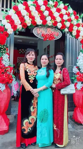 Ba phụ nữ mặc áo dài đứng dưới cổng hoa đám cưới.