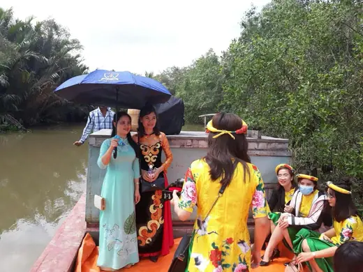 Đoàn người mặc áo dài ngồi thuyền trên sông.