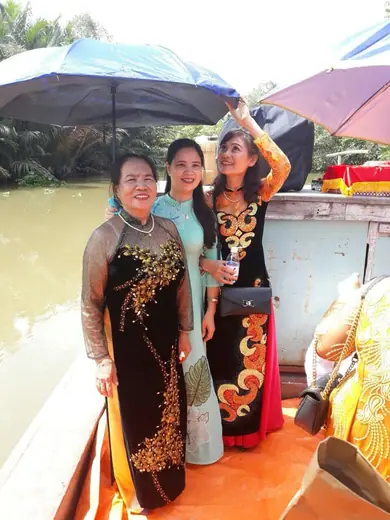 Ba phụ nữ mặc áo dài đứng trên thuyền dưới chiếc ô.