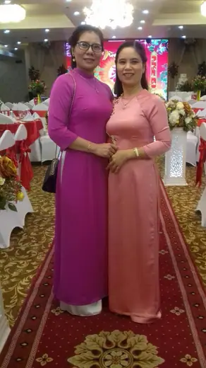 Hai phụ nữ mặc áo dài tím hồng và hồng đứng trong sảnh tiệc cưới.