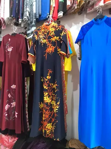 Ba chiếc áo dài treo trong tiệm: đỏ đô vẽ hoa sen, xanh đen in hoa cam và xanh dương.