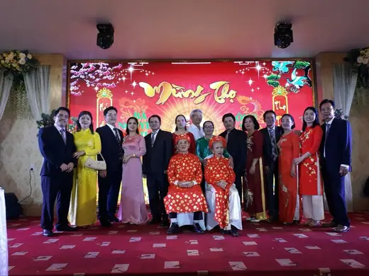 Đại gia đình mặc áo dài và vest chụp ảnh trên sân khấu lễ mừng thọ.