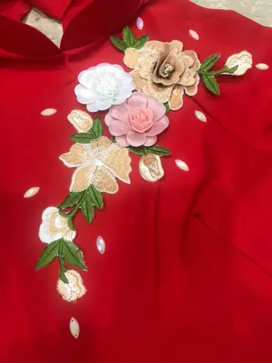 Cận cảnh hoa vải nhiều màu đính trên áo dài đỏ.