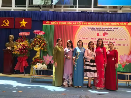 Tập thể cô giáo mặc áo dài đứng trước phông lễ tổng kết năm học.