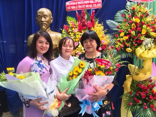 Ba cô giáo ôm hoa đứng bên lẵng hoa chúc mừng.