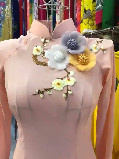 Cận cảnh hoa vải và cành hoa kết cườm trên áo dài hồng phấn.