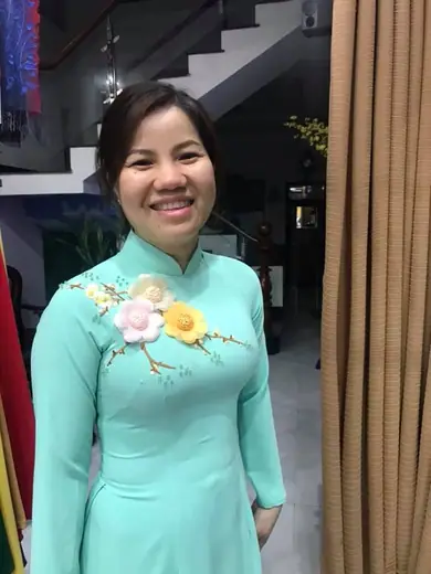 Một phụ nữ mặc áo dài xanh bạc hà đính hoa tươi cười trong tiệm.