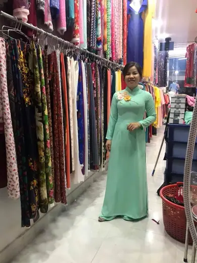 Một phụ nữ mặc áo dài xanh bạc hà đứng giữa tiệm.