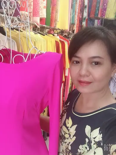Một phụ nữ chụp ảnh tự sướng bên chiếc áo dài hồng sen trong tiệm.