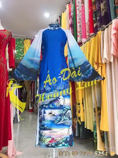 Áo dài xanh dương in tranh phong cảnh, tay loe, trên ma-nơ-canh; ảnh có logo và số điện thoại của tiệm.