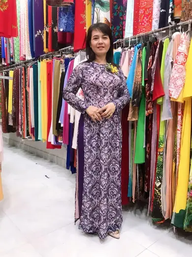 Một phụ nữ mặc áo dài tím hoạ tiết đứng trong tiệm.
