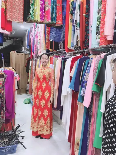Một phụ nữ mặc áo dài cưới đỏ hoạ tiết vàng đứng trong tiệm.
