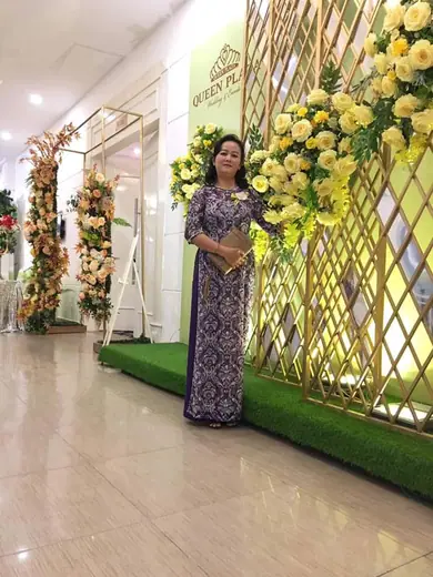 Một phụ nữ mặc áo dài tím hoạ tiết đứng bên cổng hoa trang trí.