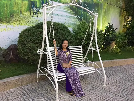 Một phụ nữ mặc áo dài tím hoạ tiết ngồi trên xích đu trong vườn.