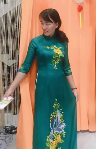 Một phụ nữ mặc áo dài xanh lục thêu chim phượng trong tiệm.