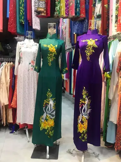 Hai chiếc áo dài xanh lục và tím thêu chim phượng trên ma-nơ-canh.