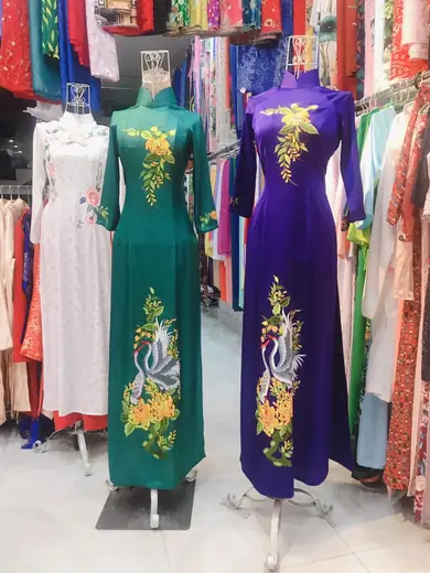 Hai chiếc áo dài xanh lục và tím thêu chim phượng trong tiệm.