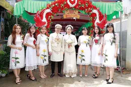 Dàn bưng quả mặc áo dài cách tân trắng in hoa chụp cùng cô dâu chú rể dưới cổng hoa.