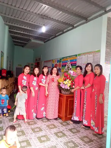 Các cô giáo mặc áo dài đỏ đứng quanh bình hoa trong sân trường.