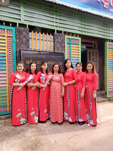 Tập thể cô giáo mặc áo dài đỏ vẽ hoa trước cổng trường.