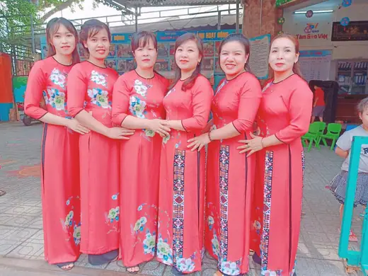 Sáu cô giáo mặc áo dài đỏ san hô vẽ hoa đứng thành hàng.