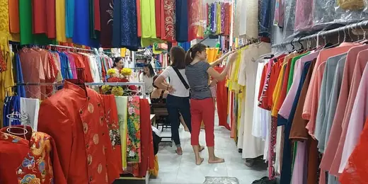 Bên trong tiệm với các sào áo dài nhiều màu và khách đang lựa.