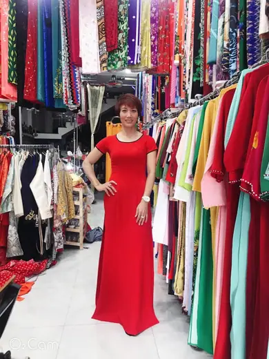 Một phụ nữ mặc đầm dài đỏ tay ngắn đứng trong tiệm.