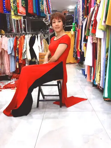 Một phụ nữ mặc đầm đỏ phối đen ngồi trên ghế giữa tiệm.