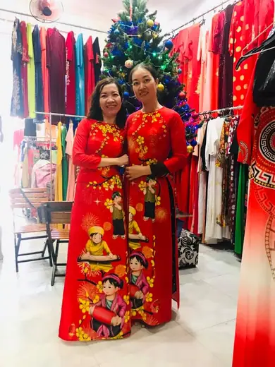 Hai phụ nữ mặc áo dài đỏ in hoạ tiết Tết đứng trong tiệm bên cây thông Noel.