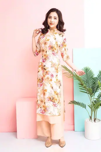 Người mẫu mặc áo dài cách tân in hoa nền kem và quần ống rộng, nền hồng.