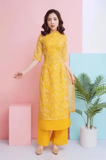 Người mẫu mặc bộ áo dài cách tân ren vàng và quần vàng, nền hồng.