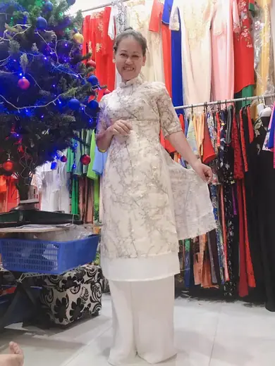 Một phụ nữ mặc áo dài cách tân ren kem và quần trắng trong tiệm.