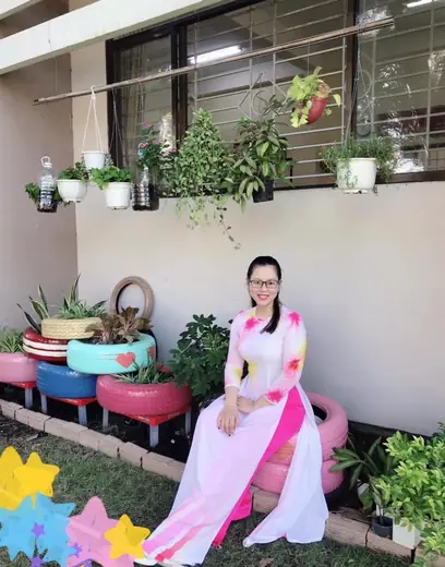 Một phụ nữ mặc áo dài trắng phối hồng ngồi bên bồn hoa trang trí.