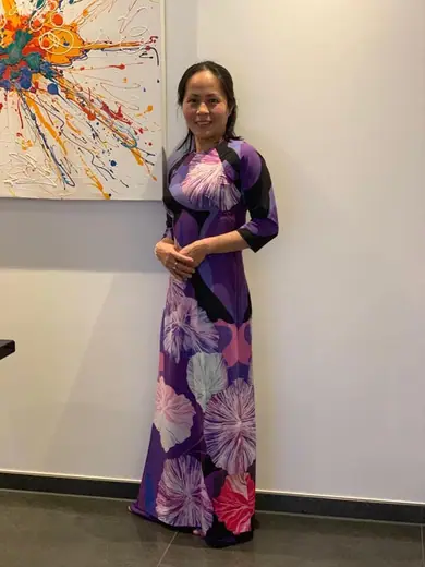 Một phụ nữ mặc áo dài tím in hình lá đứng trước bức tranh trừu tượng.
